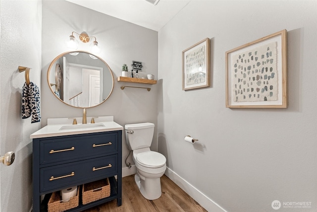 half bathroom featuring toilet, vanity, baseboards, and wood finished floors