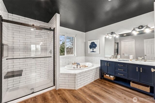 full bath featuring a garden tub, double vanity, wood finished floors, and a stall shower