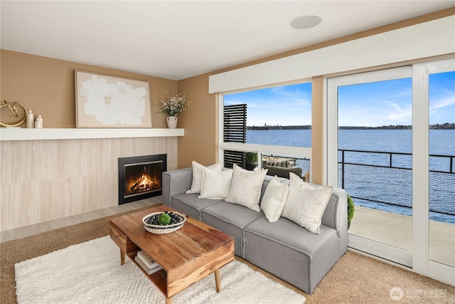 carpeted living room with a water view and a fireplace with flush hearth