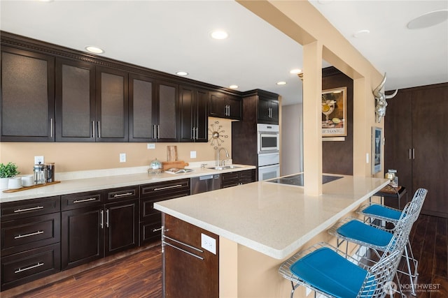 kitchen featuring a kitchen breakfast bar, black electric stovetop, stainless steel dishwasher, and dark wood-type flooring