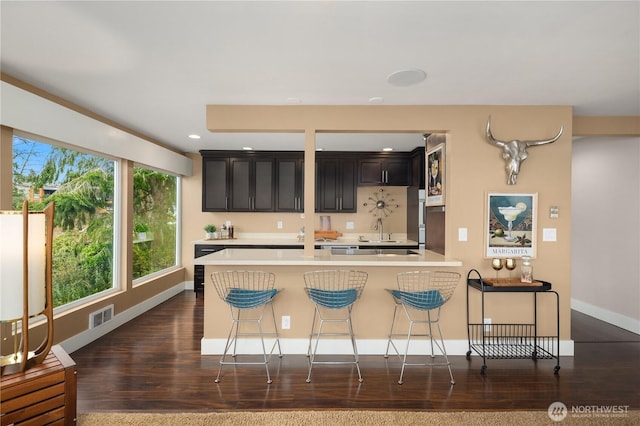 kitchen with visible vents, a sink, light countertops, dark wood-type flooring, and a kitchen bar