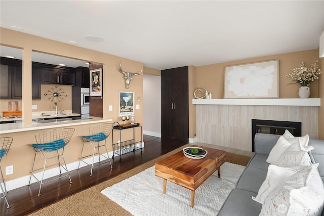 living area featuring baseboards, a glass covered fireplace, and dark wood-style flooring