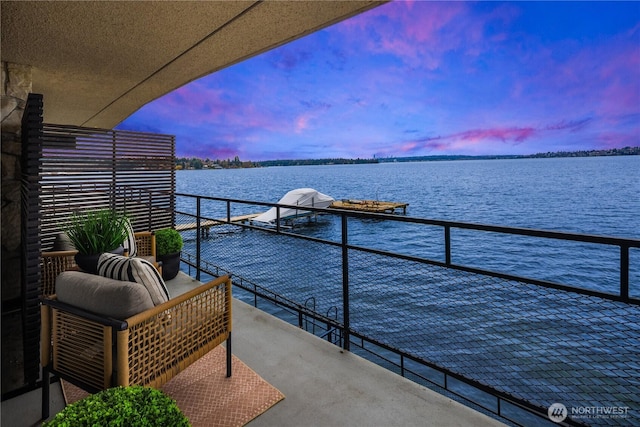 balcony at dusk featuring a water view and a boat dock