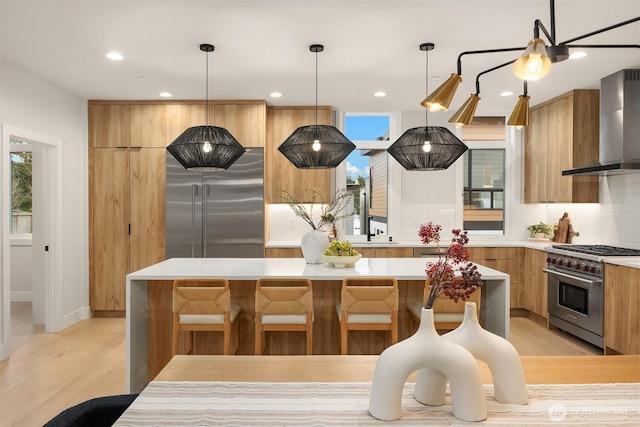 kitchen with modern cabinets, premium appliances, wall chimney range hood, a center island, and light countertops