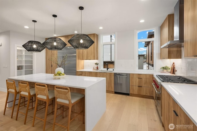 kitchen featuring modern cabinets, a sink, stainless steel appliances, a breakfast bar area, and wall chimney exhaust hood