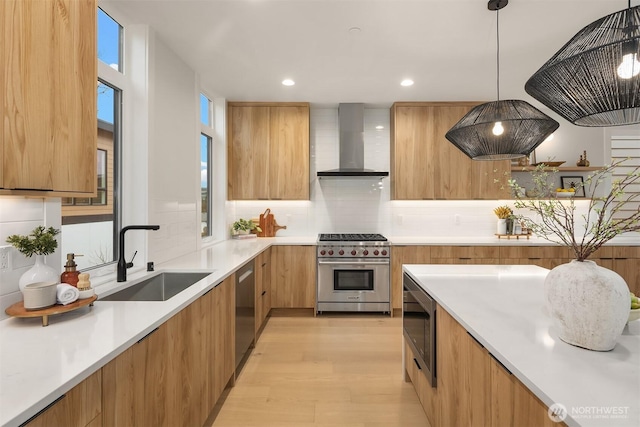 kitchen with wall chimney range hood, light countertops, appliances with stainless steel finishes, modern cabinets, and a sink