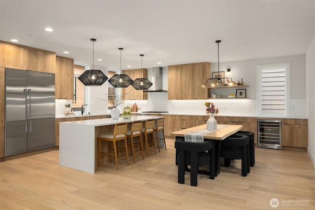 kitchen featuring light wood finished floors, wall chimney range hood, beverage cooler, appliances with stainless steel finishes, and modern cabinets