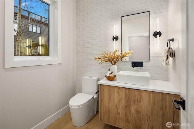 bathroom featuring backsplash, baseboards, toilet, wood finished floors, and vanity