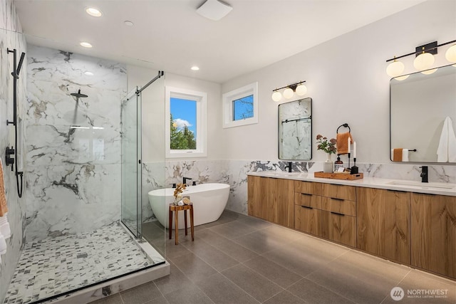 bathroom featuring a sink, a marble finish shower, tile walls, double vanity, and a freestanding bath