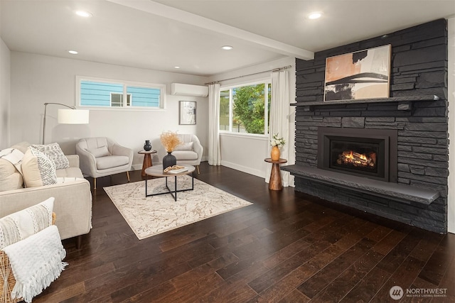 living room with beam ceiling, an AC wall unit, wood finished floors, a stone fireplace, and baseboards