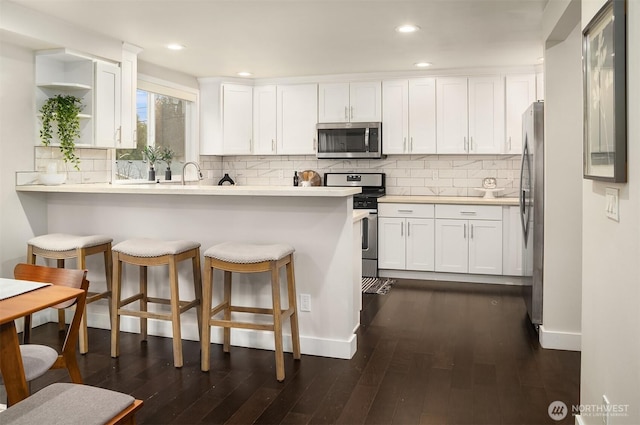 kitchen featuring a breakfast bar area, a peninsula, dark wood-type flooring, appliances with stainless steel finishes, and white cabinetry