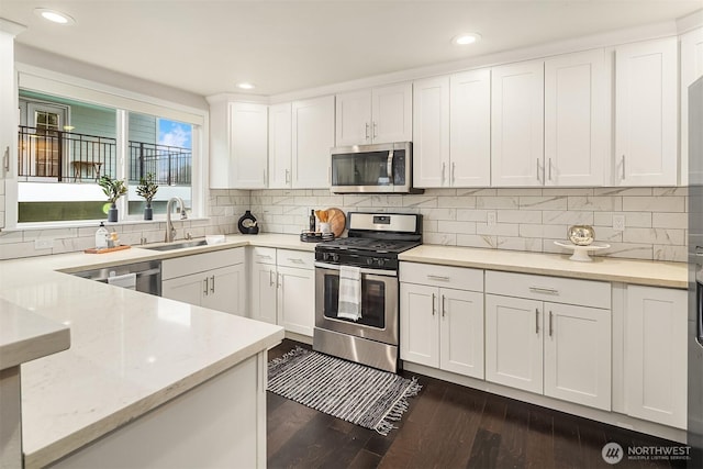 kitchen featuring dark wood-style floors, a sink, stainless steel appliances, white cabinetry, and backsplash