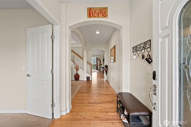 foyer featuring arched walkways, stairs, light wood-type flooring, and baseboards