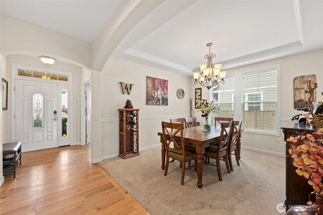 dining room with light wood-style floors, a raised ceiling, a notable chandelier, and arched walkways