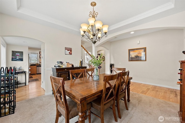 dining space featuring light carpet, ornamental molding, arched walkways, a raised ceiling, and stairs