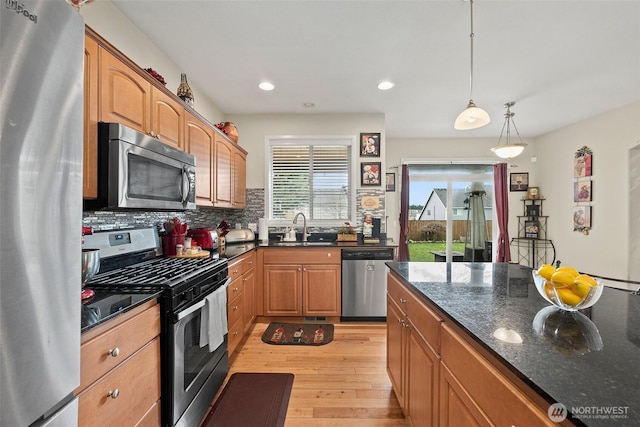 kitchen featuring light wood-style flooring, a sink, decorative backsplash, hanging light fixtures, and appliances with stainless steel finishes