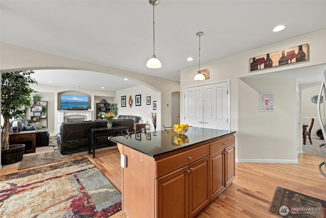 kitchen with a center island, brown cabinetry, light wood-style flooring, a fireplace, and arched walkways