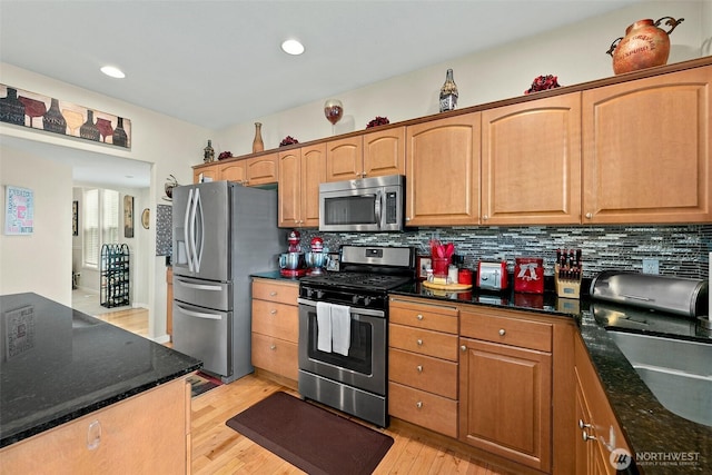 kitchen featuring decorative backsplash, dark stone countertops, light wood-type flooring, and appliances with stainless steel finishes