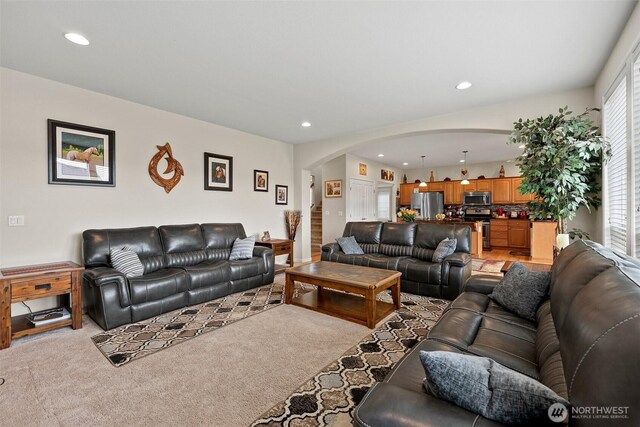 living room featuring arched walkways, stairway, recessed lighting, and light carpet