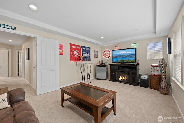 living room featuring baseboards, a tray ceiling, recessed lighting, a glass covered fireplace, and light colored carpet