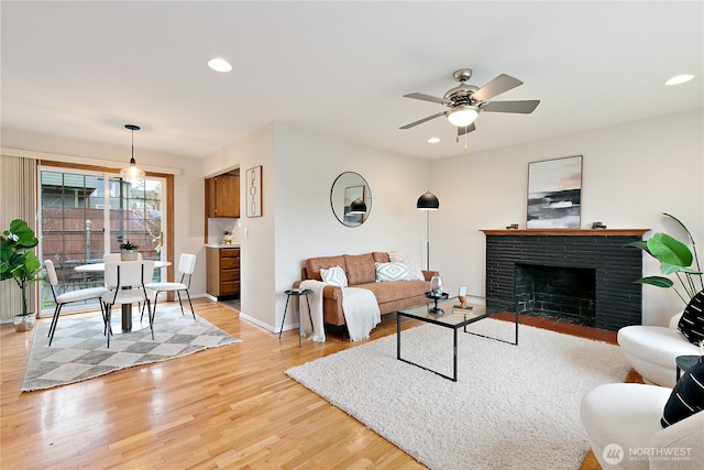 living area featuring a brick fireplace, baseboards, light wood-type flooring, recessed lighting, and a ceiling fan