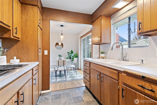 kitchen featuring brown cabinetry, stovetop, a sink, light countertops, and pendant lighting