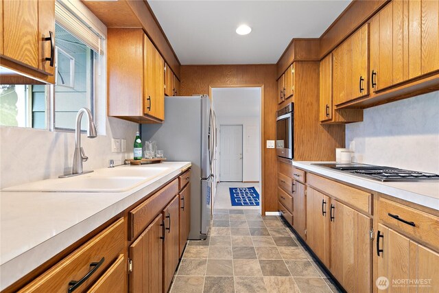 kitchen featuring brown cabinets, stainless steel appliances, light countertops, and a sink