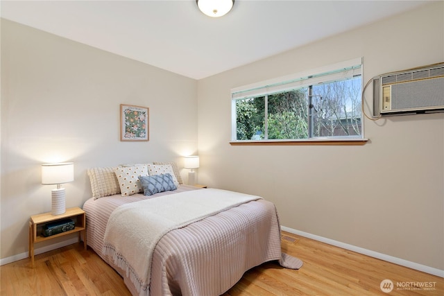 bedroom featuring visible vents, baseboards, a wall unit AC, and wood finished floors