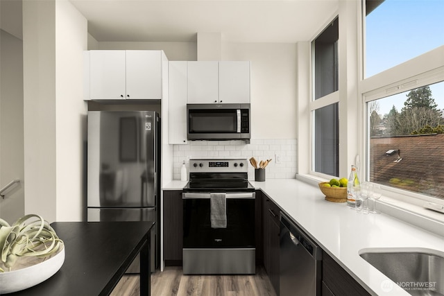 kitchen with backsplash, white cabinetry, stainless steel appliances, light wood-style floors, and light countertops