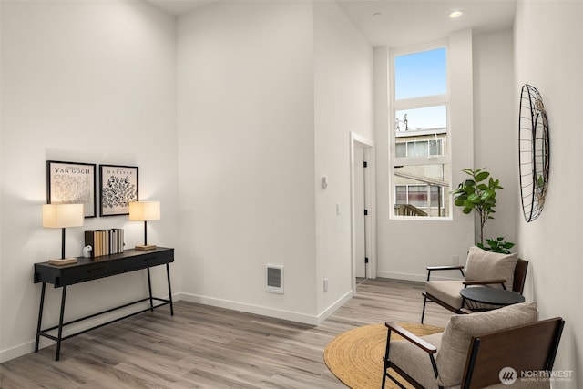 sitting room with baseboards, wood finished floors, and a towering ceiling