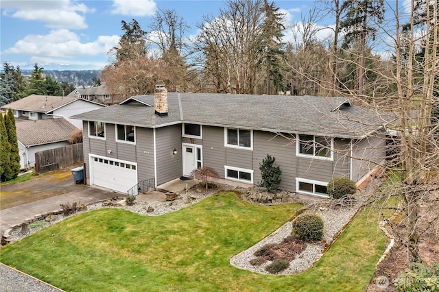 raised ranch with a shingled roof, a front yard, a chimney, a garage, and driveway