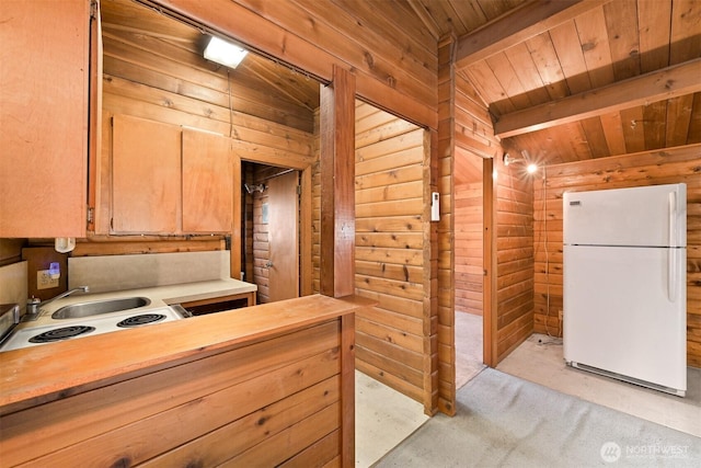 kitchen with a sink, wood walls, wooden ceiling, and freestanding refrigerator