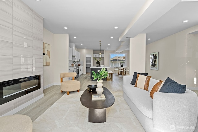 living room featuring recessed lighting, baseboards, light wood finished floors, and a large fireplace