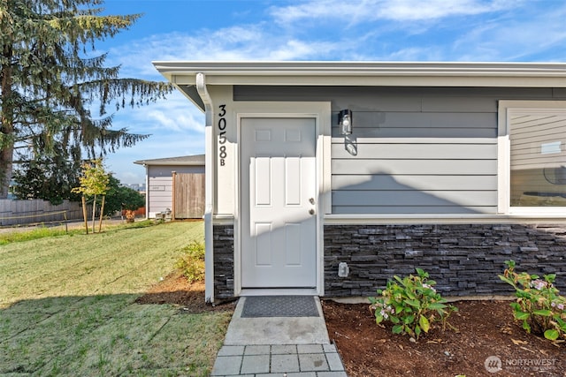 entrance to property featuring stone siding, a yard, and fence