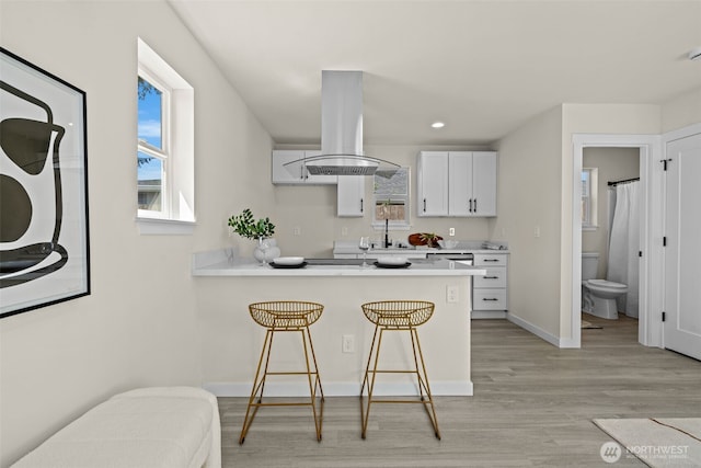 kitchen featuring a breakfast bar, light countertops, light wood-style flooring, and island exhaust hood