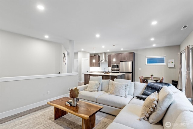 living room with recessed lighting, visible vents, baseboards, and light wood-style flooring