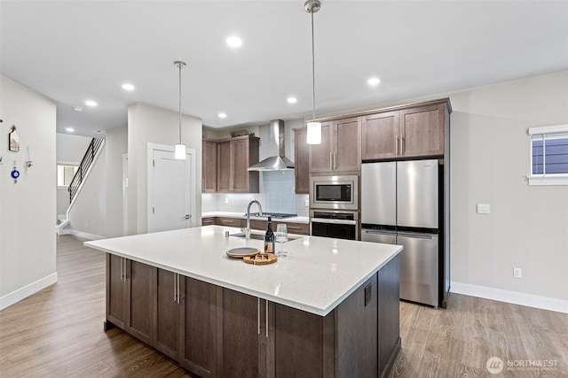 kitchen with light wood-style flooring, backsplash, appliances with stainless steel finishes, and wall chimney exhaust hood