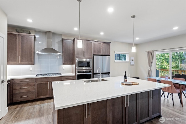 kitchen with a sink, light wood-style flooring, wall chimney exhaust hood, and stainless steel appliances