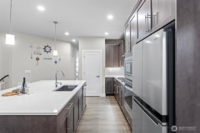 kitchen featuring light wood finished floors, recessed lighting, a sink, dark brown cabinets, and appliances with stainless steel finishes