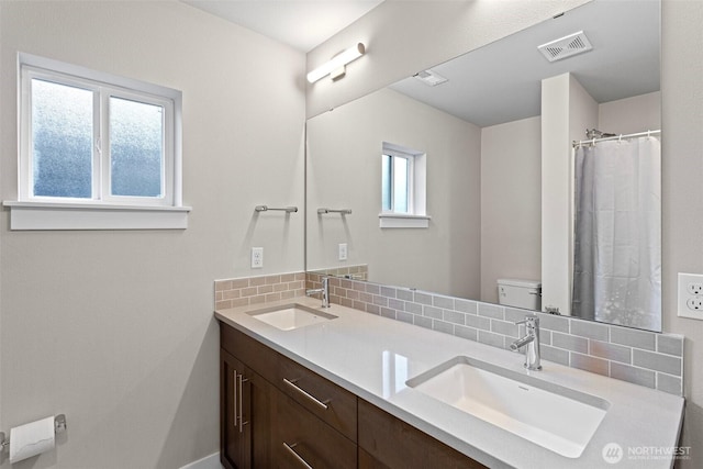 full bathroom with double vanity, toilet, visible vents, and a sink