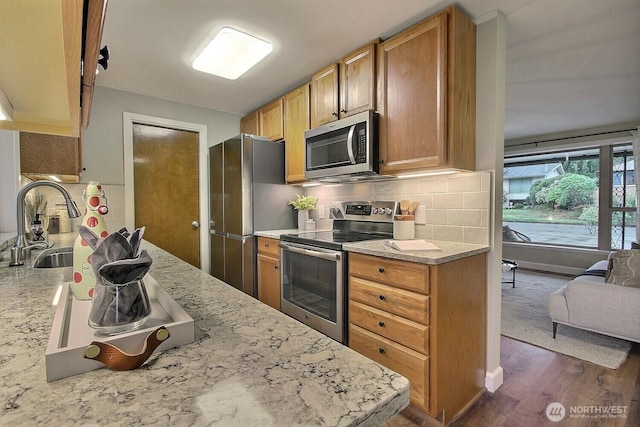 kitchen featuring light stone counters, dark wood-style floors, a sink, appliances with stainless steel finishes, and backsplash