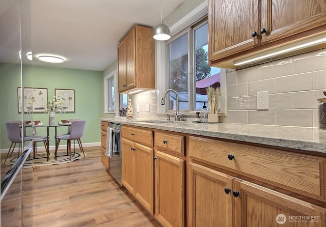 kitchen with light stone countertops, a sink, stainless steel dishwasher, light wood-type flooring, and backsplash