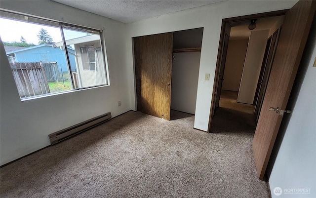 unfurnished bedroom featuring a baseboard heating unit, a textured ceiling, a closet, and carpet