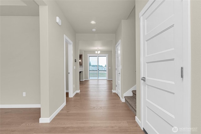 hallway featuring light wood-type flooring, baseboards, a chandelier, and stairs