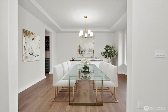 dining area with a raised ceiling, wood finished floors, baseboards, and a chandelier