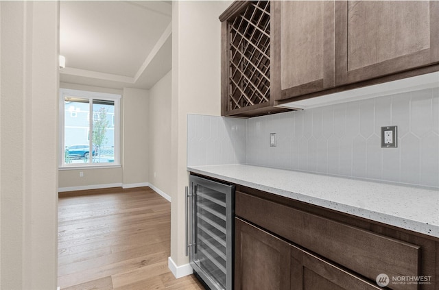 bar with beverage cooler, baseboards, light wood-style flooring, a bar, and decorative backsplash