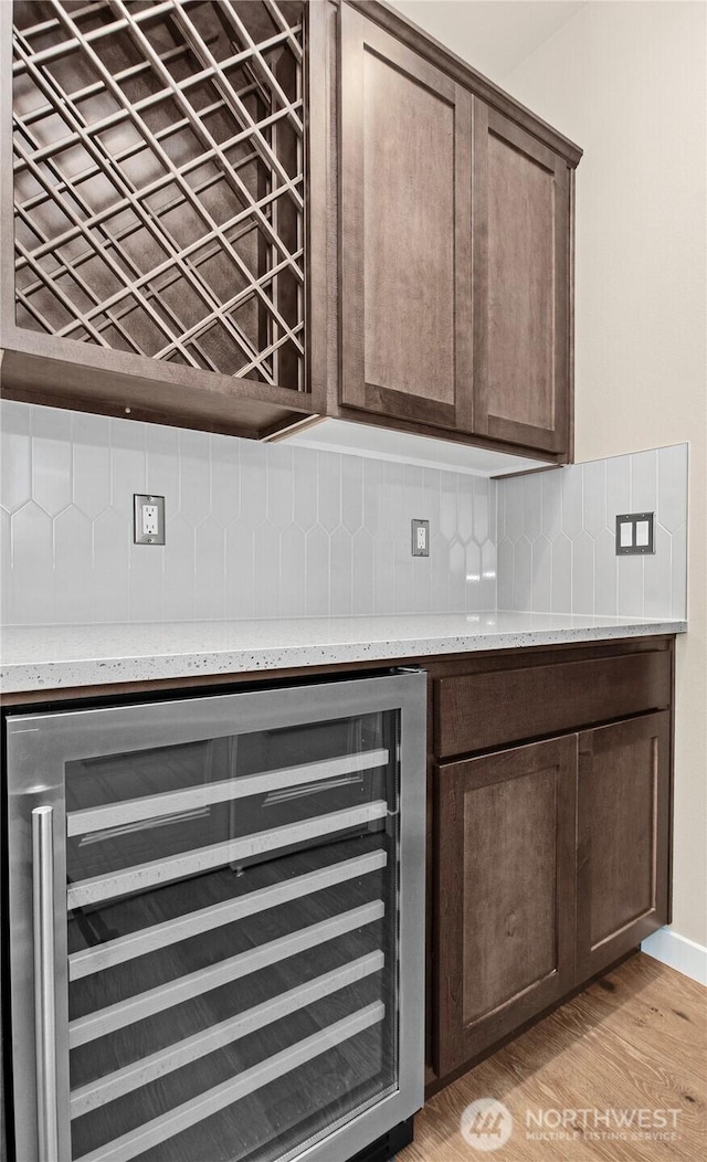 room details with light wood-style flooring, decorative backsplash, a bar, wine cooler, and dark brown cabinets