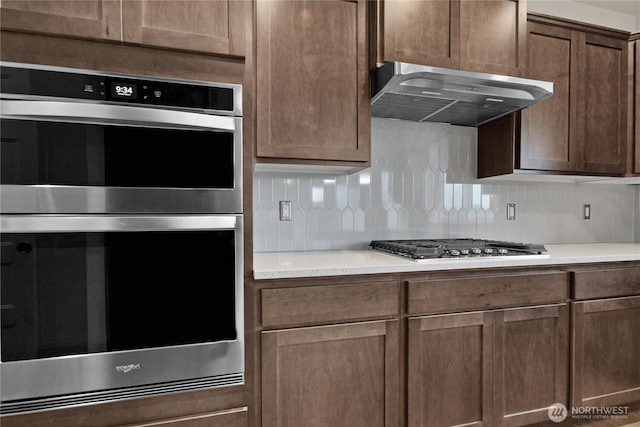 kitchen featuring under cabinet range hood, backsplash, appliances with stainless steel finishes, and light countertops