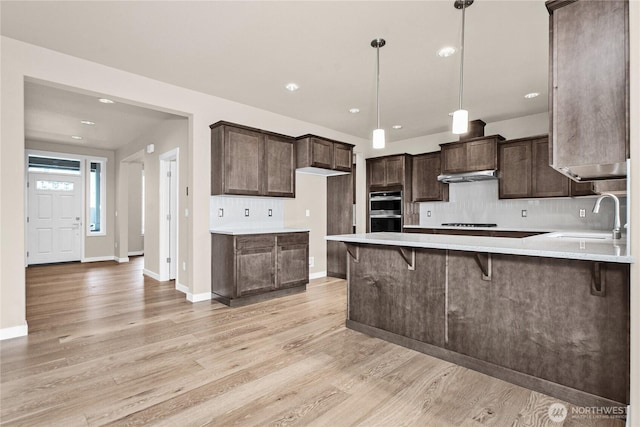 kitchen with a sink, dark brown cabinetry, double oven, light wood-type flooring, and backsplash