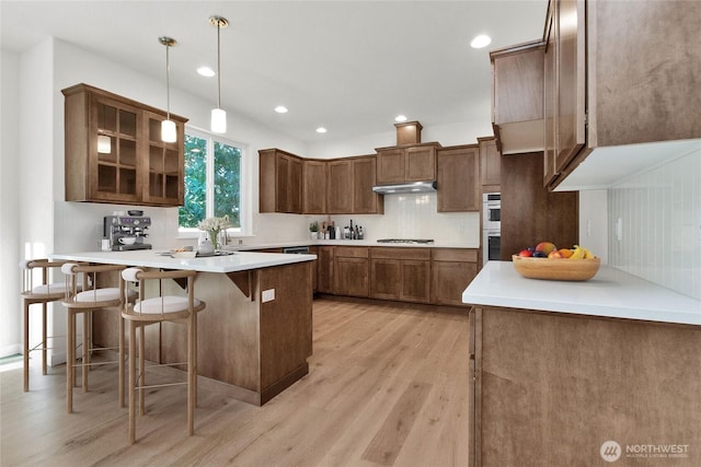 kitchen featuring under cabinet range hood, double oven, light wood-type flooring, a peninsula, and a kitchen breakfast bar